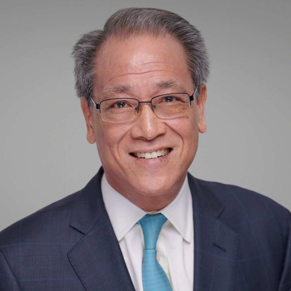Kenneth Mendez smiling in a picture on a grey background and in a navy suit