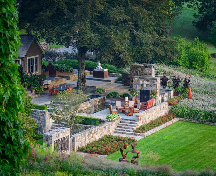 A landscaped garden with a lawn next to a dining area with stone steps and a wall