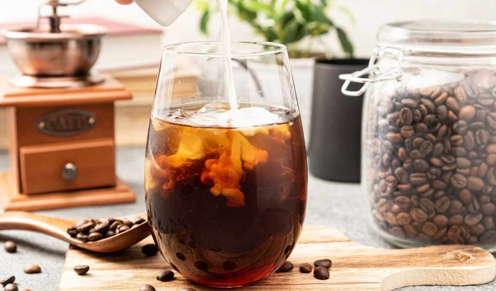 A glass container showing milk being poured into a coffee