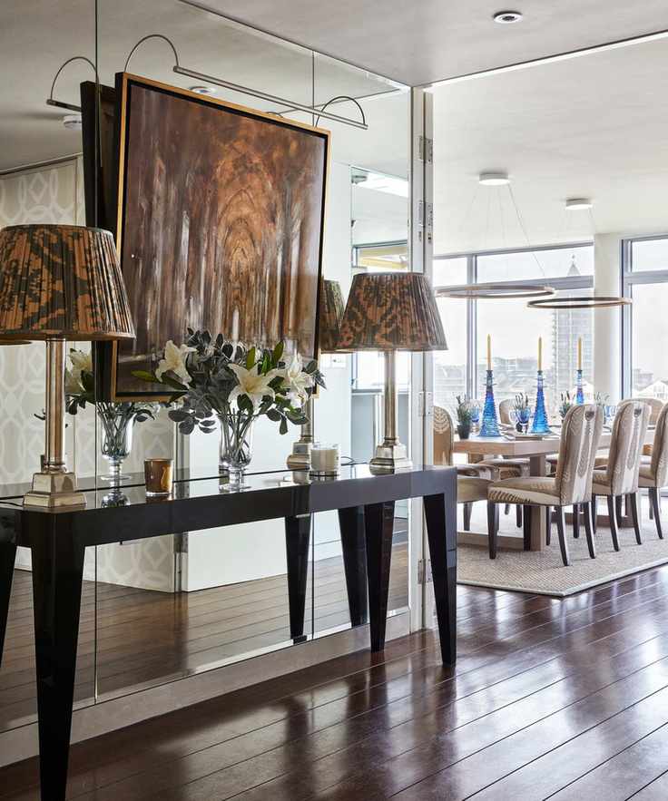 A hallway lighting idea with table lamps on a console table, backed onto a mirrored wall