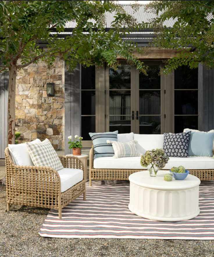 Outdoor living room with rattan furniture, blue patterned throw pillows, a white coffee table and striped rug
