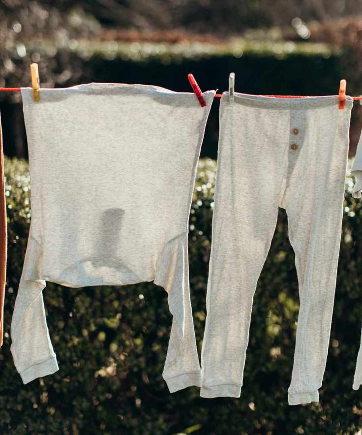 A clothes line hung outside in front of a green hedge with orange and white cotton pyjamas hanging from it