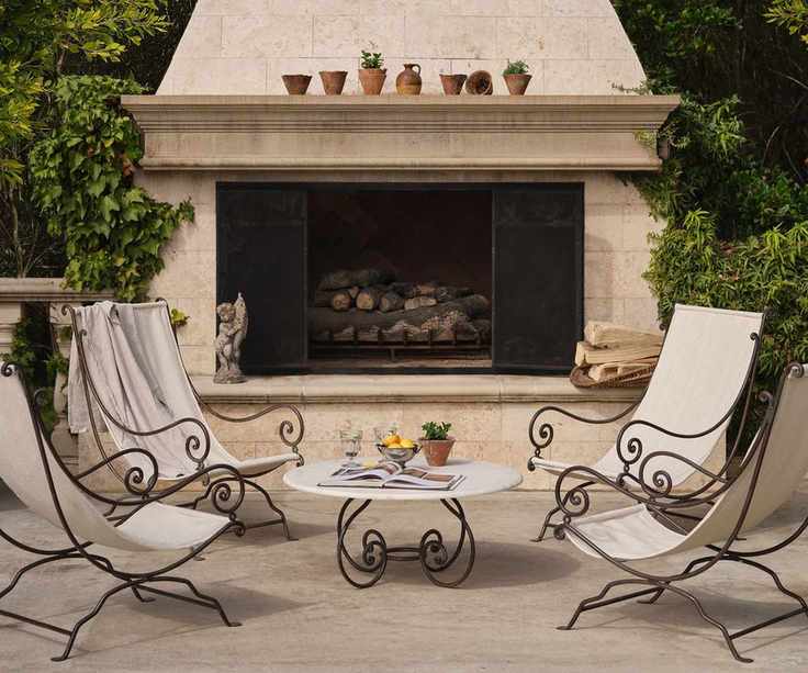 large patio with a huge stone outdoor fireplace with wrought iron and canvas deck chairs and a matching curved round coffee table