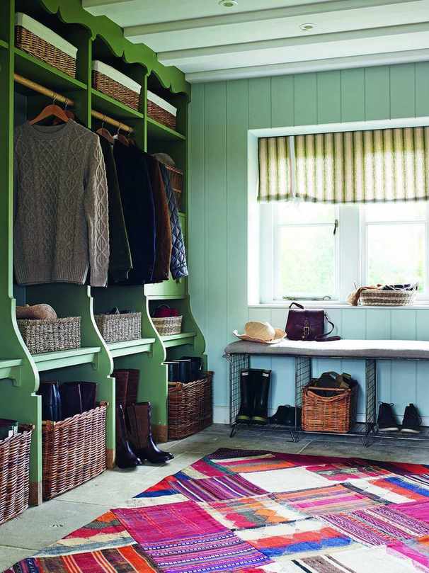 An example of mudroom ideas showing a brightly patterned floor rug and green storage with wicker baskets