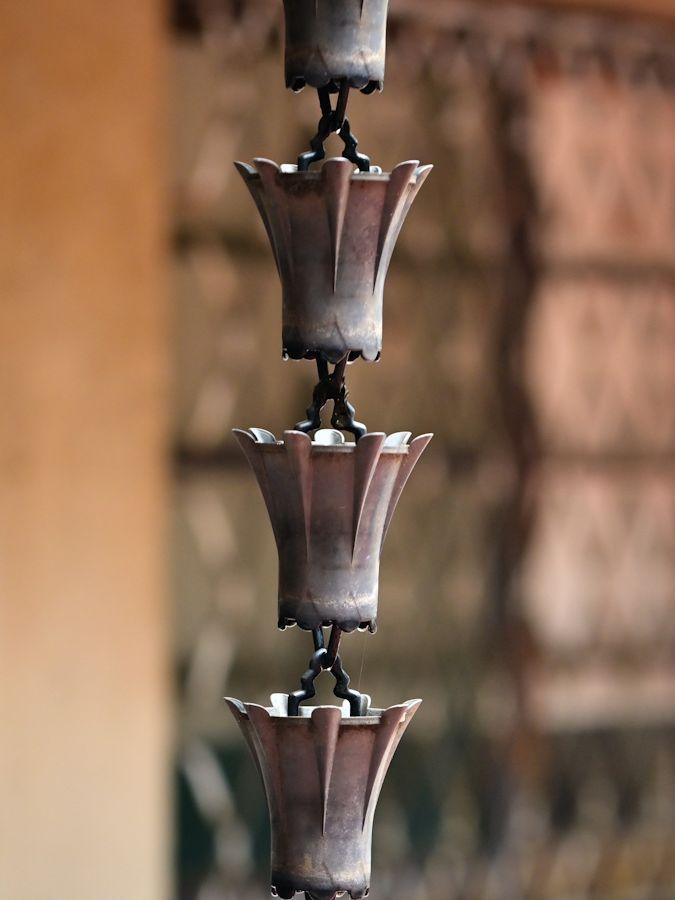 Traditional rain chain drainage system featuring series of connected cup-shaped or funnel-shaped metal containers