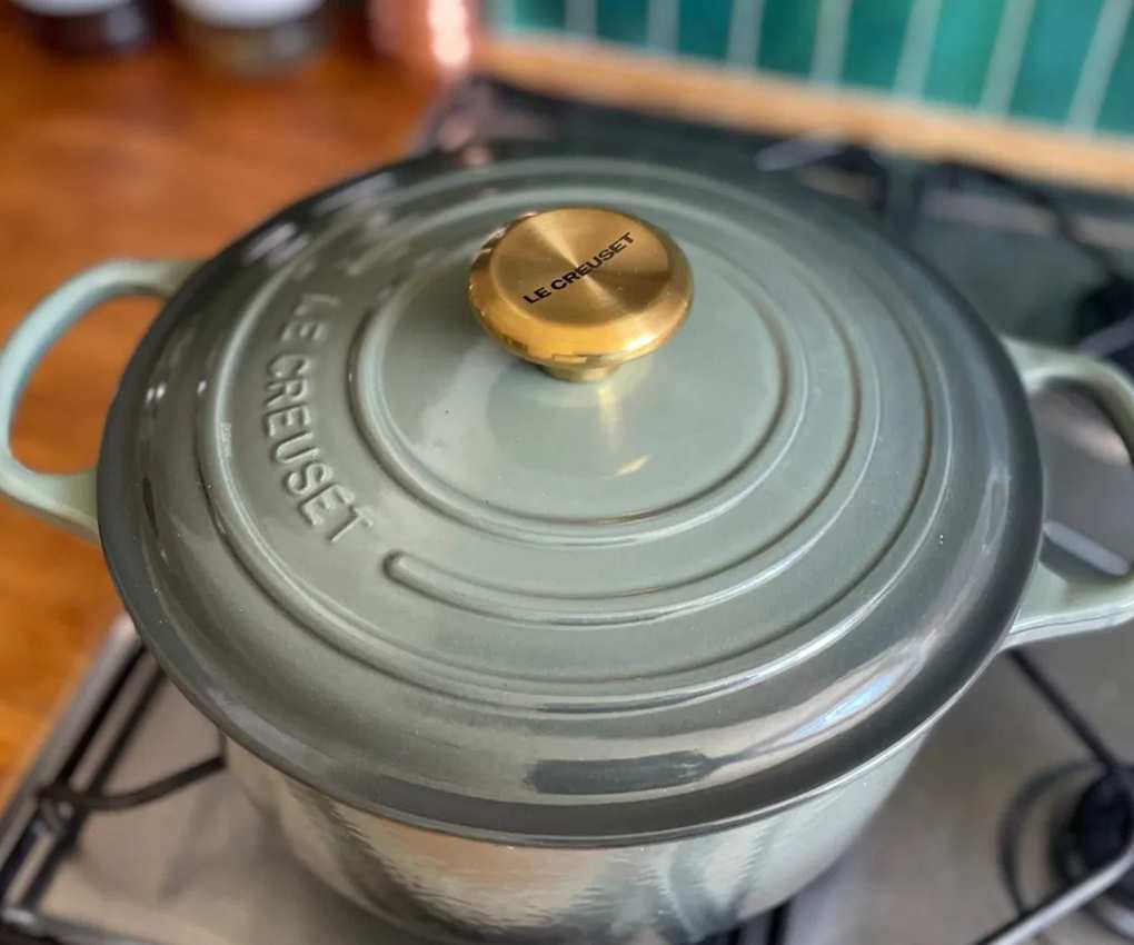 Le Creuset Dutch oven in the dusty green 'Thyme' colorway on a gas stove.