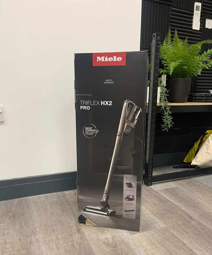 Miele Triflex HX2 Pro original packaging on laminate floor in front of shelves and plants