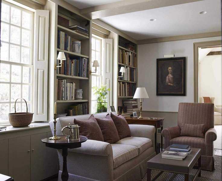 A library with custom built bookshelves and shutters and neutral walls and upholstery