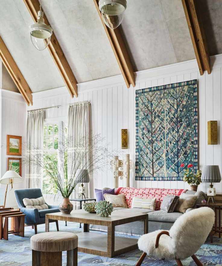 A bright, airy living room with vaulted wood-beamed ceilings, white wood-paneled walls, and a large blue tree-patterned wall hanging