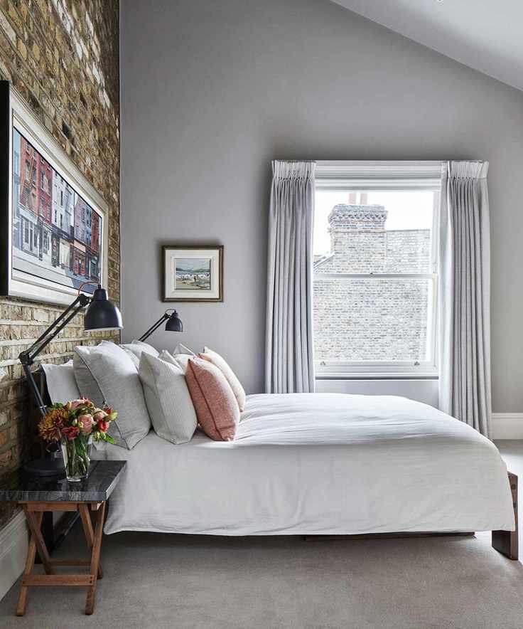 Exposed brick accent wall in a soft gray bedroom with white bedding and black lamps on either side of the bed.
