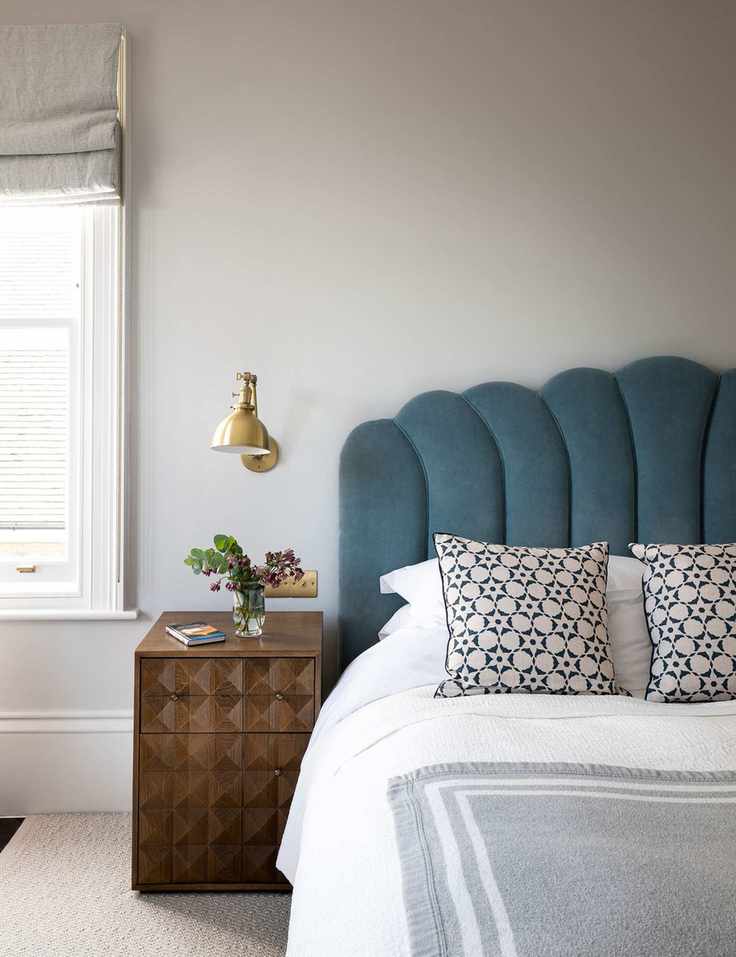 Grey bedroom with scalloped headboard and wall lamp