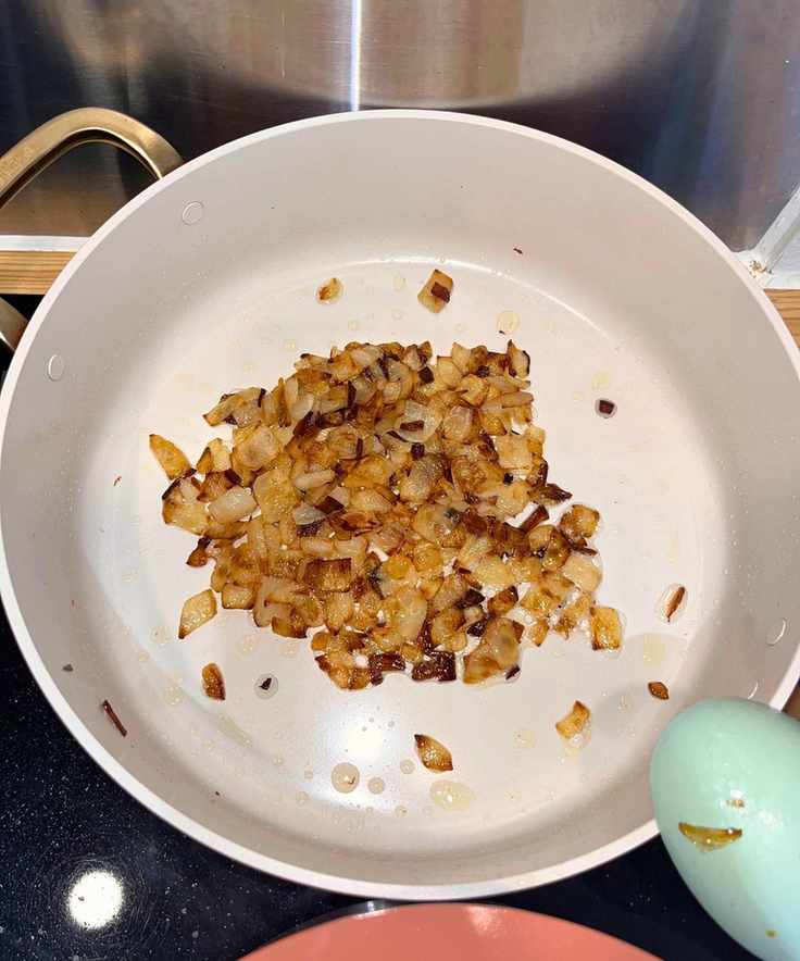 Frying onions in the Our Place frying pan from the Essentials 11-Piece Set. Most are golden-caramel color, and some are darker
