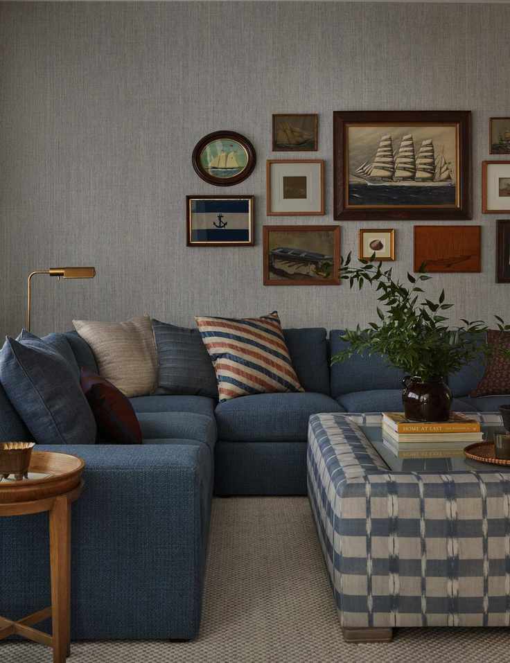 Living area featuring a blue sectional, patterned ottoman, and maritime artwork