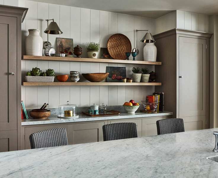Open kitchen shelving holding crockery, books and lamps in a neutral kitchen