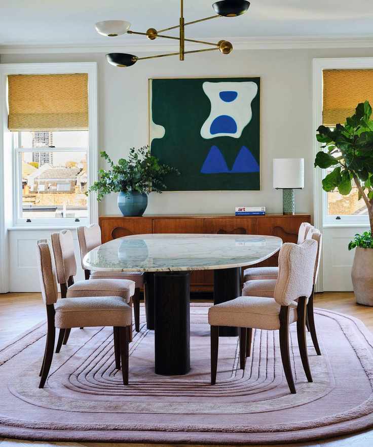 a white dining room with yellow window blinds, a large curved lilac rug, marble dining table, curved chairs and large green abstract art