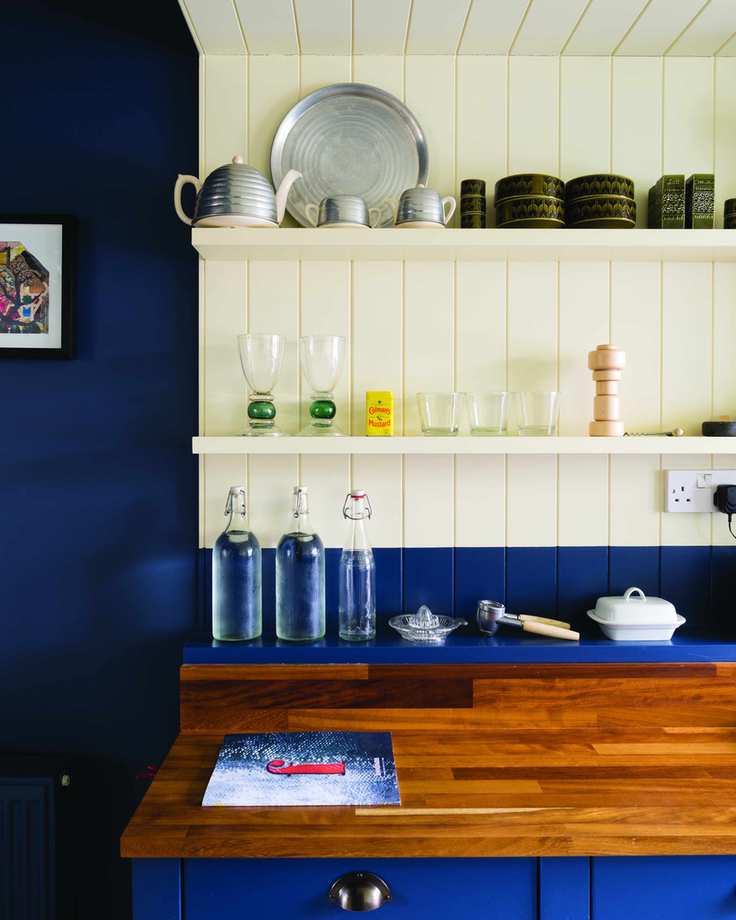 Deep blue kitchen walls, a white wall and shelf and cherry wood worktops.