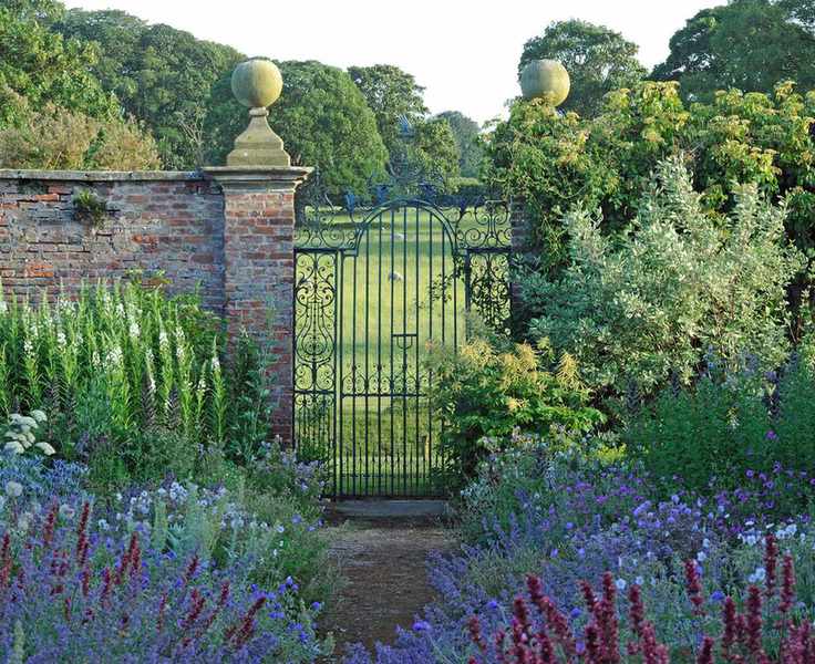 Wrought iron gate flanked by brick wall and cottage-style deep flower beds.