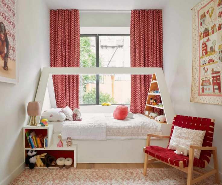 Girls' bedroom with red printed curtains, single wood bed with a white roof, pink floral carpet, wood armchair with red weave and white open shelving