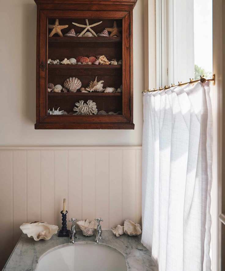 Classic bathroom with shiplap half walls, cafe style curtain, marble topped basin, vintage wall cabinet