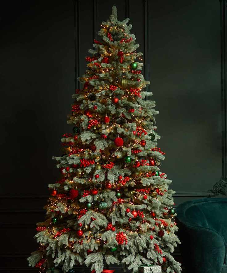 A christmas tree with green and red decorations against a dark green wall with a dark green velvet sofa to the right