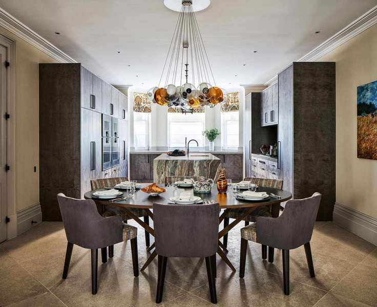 View from the dining area to the kitchen, dramatic central light above round table, tiled floor and central kitchen island.