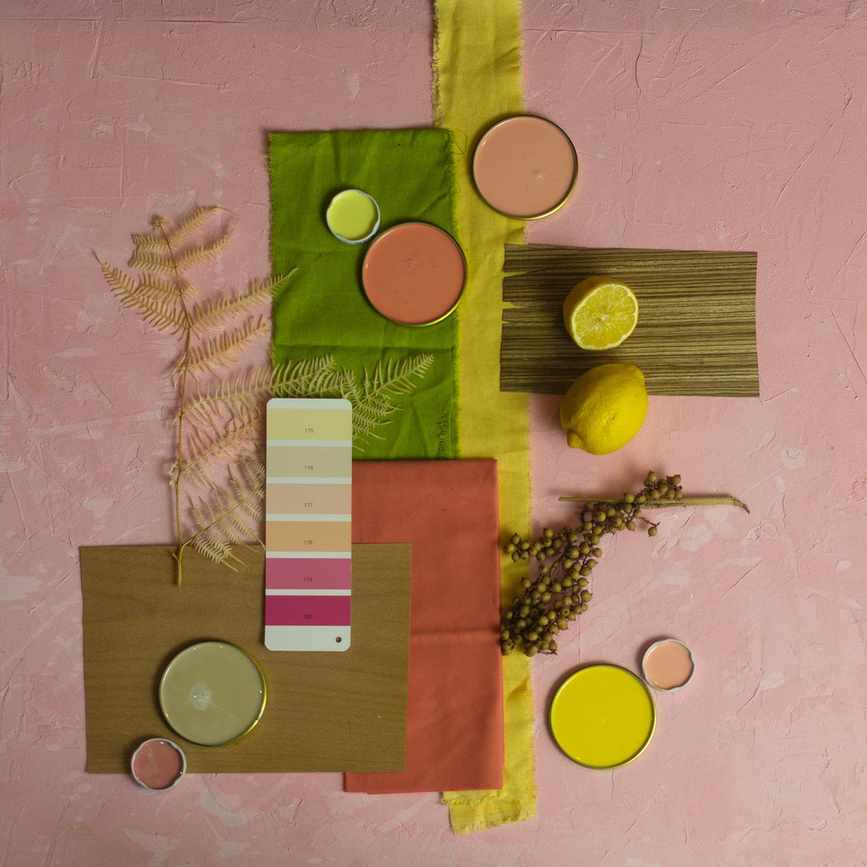 colorful moodboard on pink plaster background with green and yellow fabric and pink and yellow paints along with other accessories