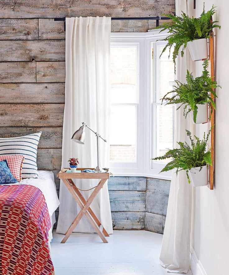 Bedroom ideas for teenagers with rustic gray-washed wood panels, house plants and red patterned bed throw.
