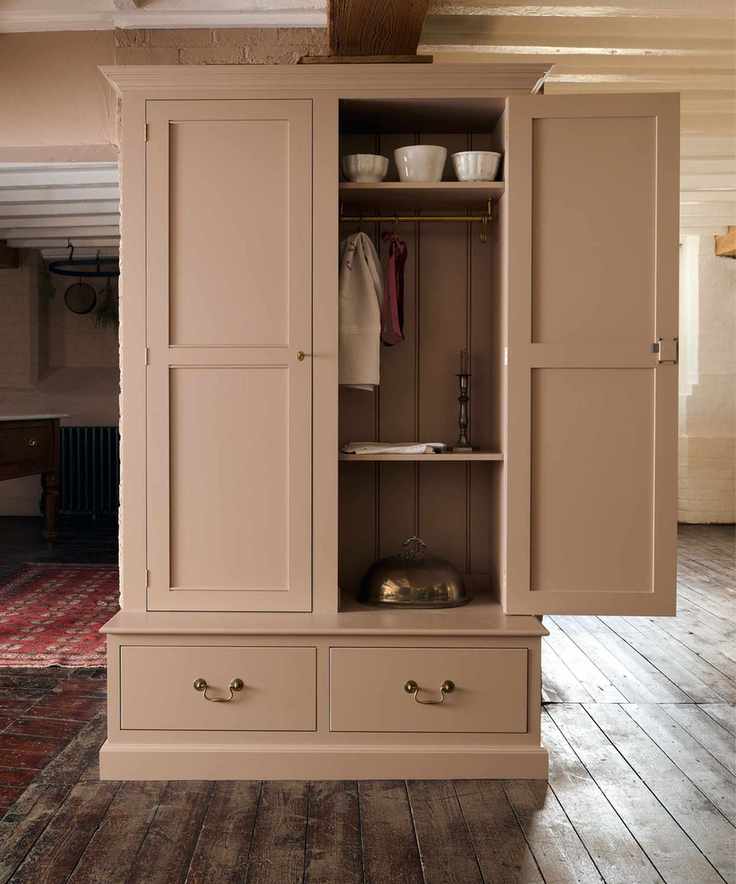 Freestanding pale blush pink pantry with open door on dark original hardwood floors in rustic cottage kitchen. There’s a red rug in left background