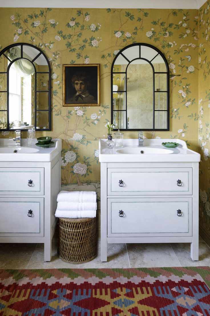 Striking yellow flowery wallpaper, black framed mirrors, vibrant patterned rug and white twin sinks
