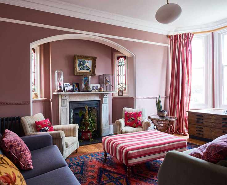 Pink painted living room featuring a bright bay window, navy sofa, cream striped armchairs, and a pink striped ottoman, all paired with matching striped curtains.