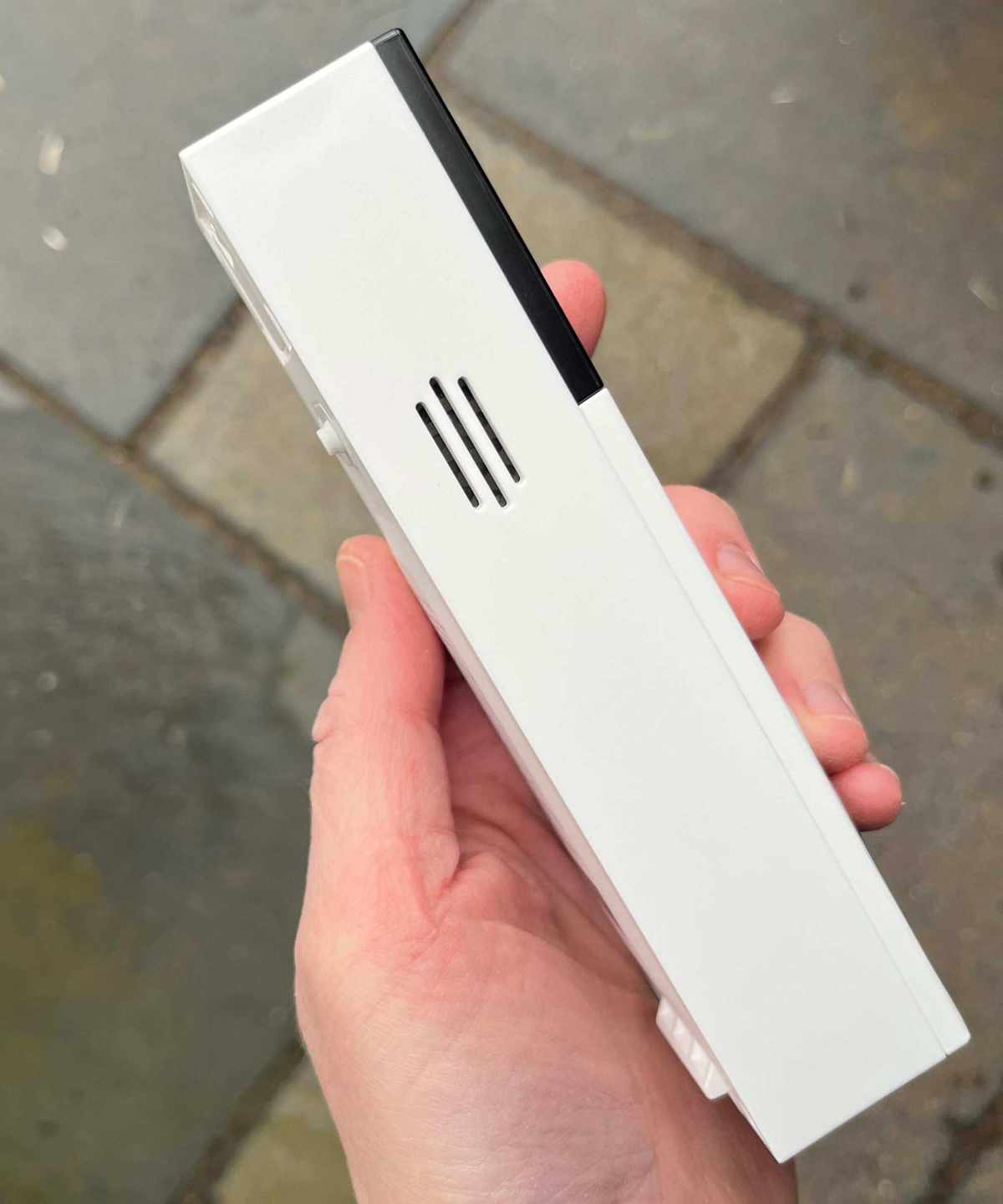 Hand holding the Tapo D210 Video Doorbell, showing the device's side, above tiled concrete floor.