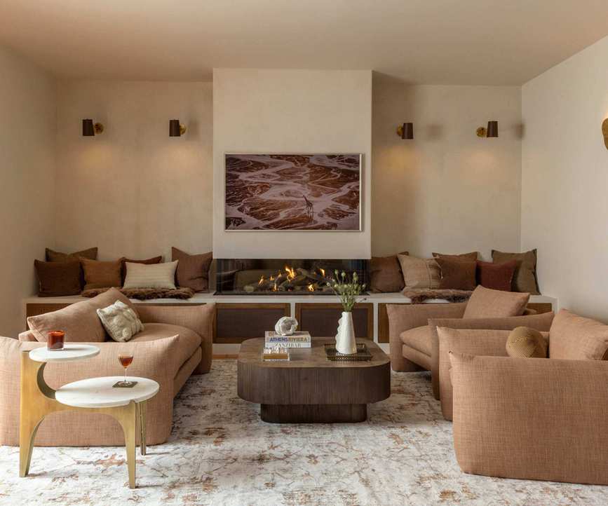 neutral warm minimalist living room with a chimney breast and lit fire, nook seating and armchairs and sofa in a soft terracotta