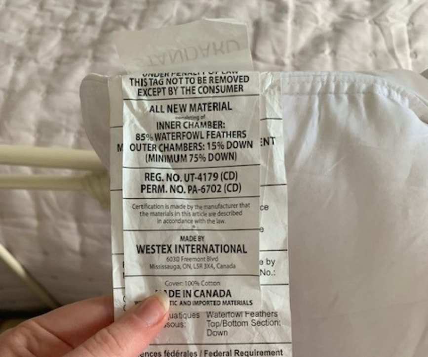 A hand holding the care tag on the Brooklinen Down Pillow.