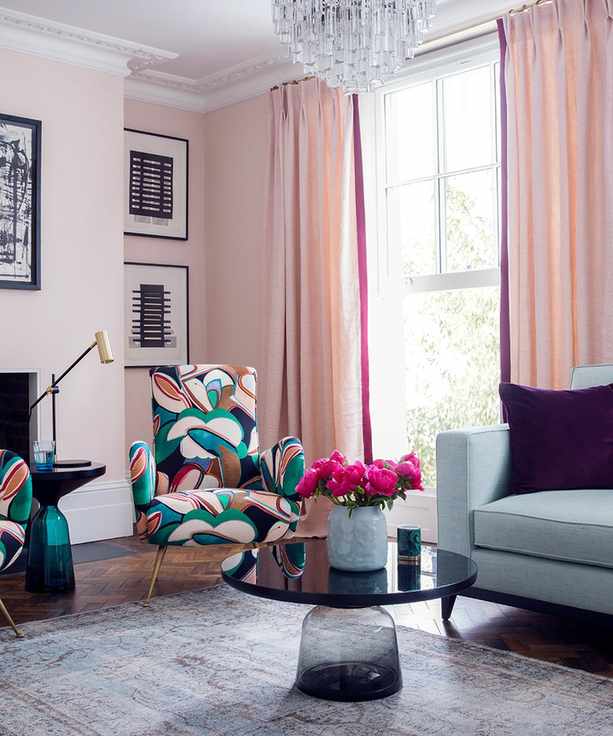 A pink living room with glass chandelier and abstract floral print chairs.