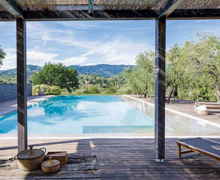 The view of a pool surrounded by trees from under a pergola with decking
