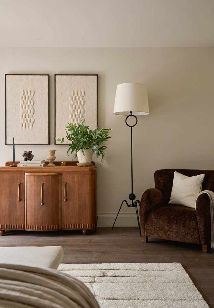 A mic-century style bedroom with a cream rug, a wooden side table, and a brown armchair next to a floor lamp