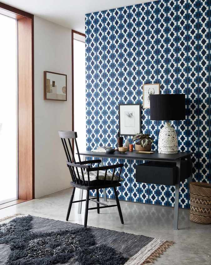 Home office with desk and chair, blue and white geometric wallpaper on one wall, and neutral floor and wall, and rug