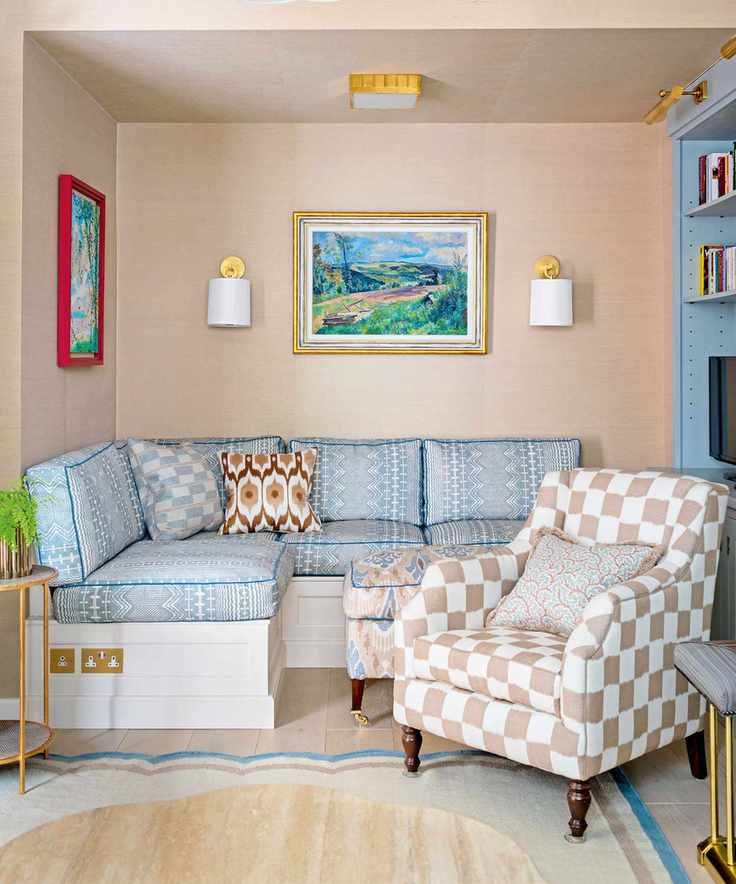 Small living room with blue patterned sofa, checkered armchair, artwork and wall lights on walls, colorful rug