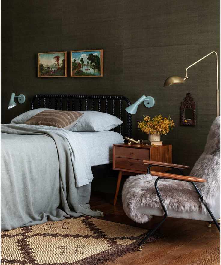 Dark olive green bedroom by Heidi Caillier design with woven wallcovering, Midcentury bedside tables, armchair with sheepskin and light blue bedside wall lamps