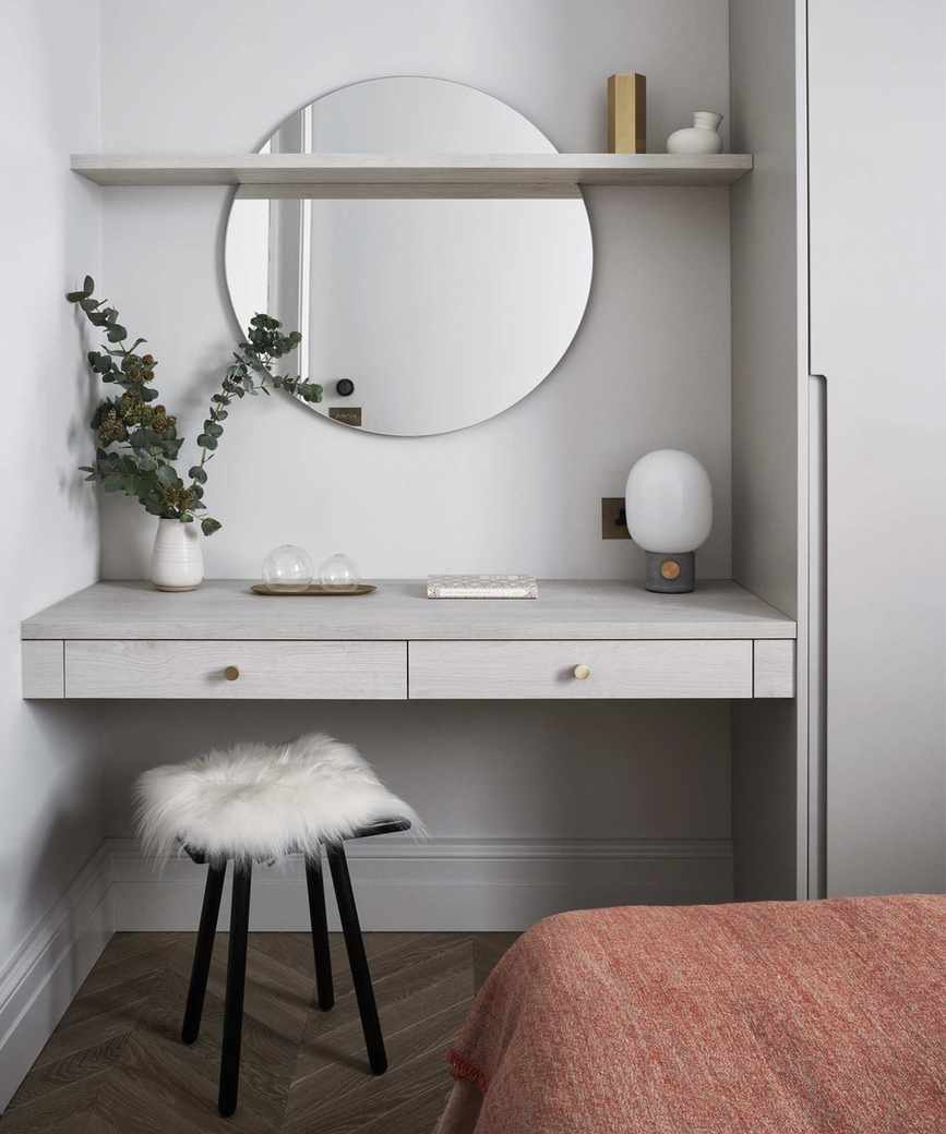 A bedroom with built-in dressing table, circular mirror and fluffy seat