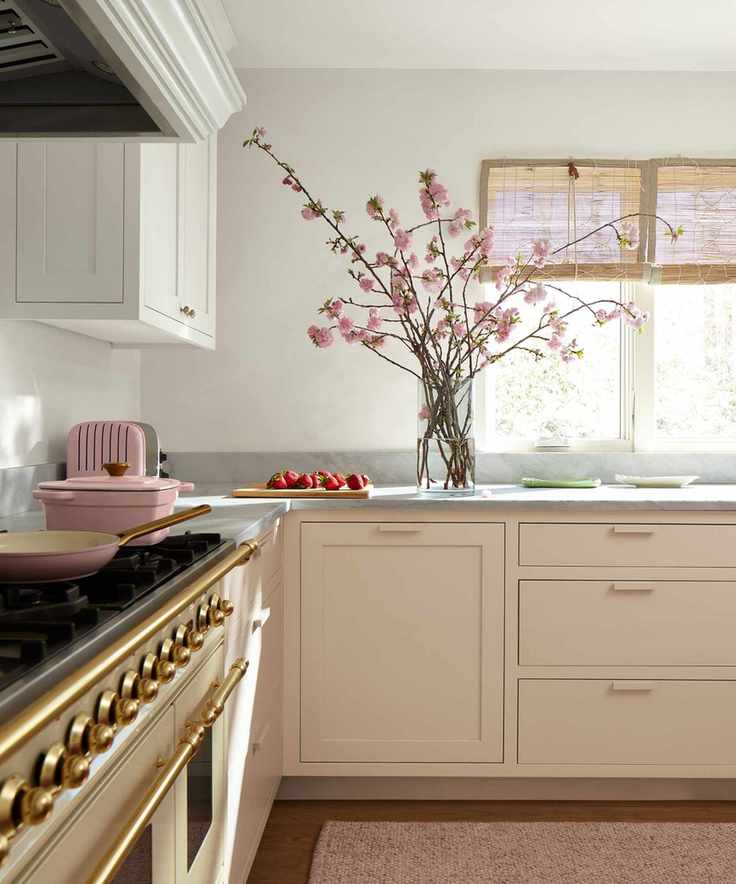 A small kitchen with pale pink cabinets, gray countertops, and warm white walls