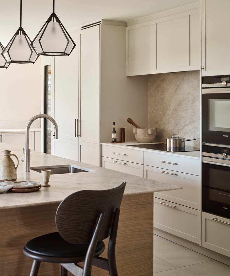 modern minimalist kitchen with white cabinets and counters. natural stone backsplash behind the glass stove top, and a matching stone island