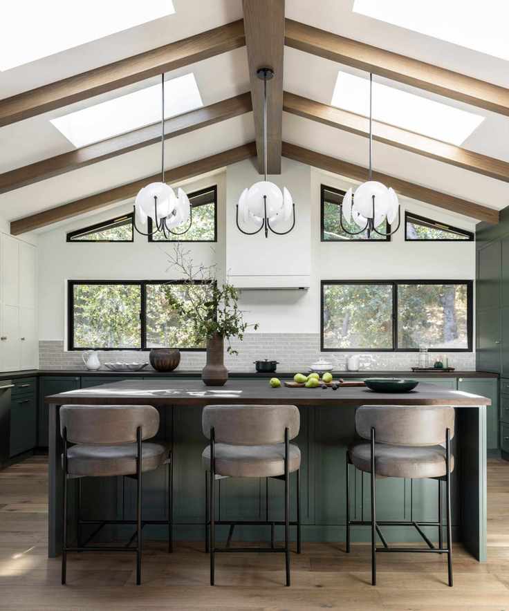 A modern kitchen featuring hanging lights, a kitchen island with stools, and a wooden floor.