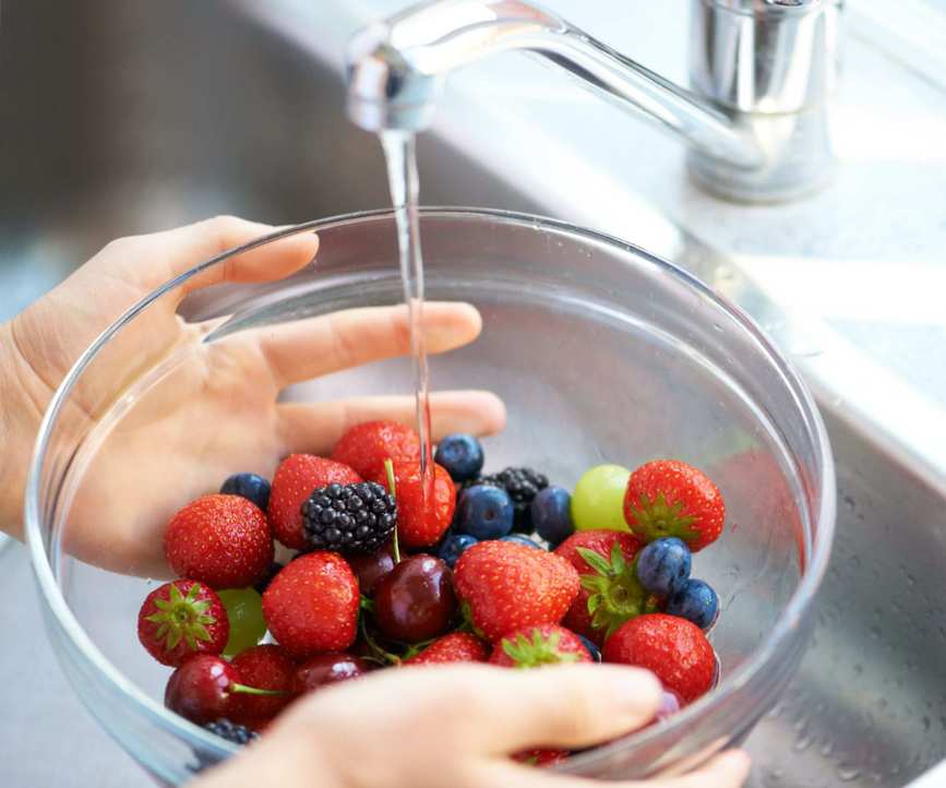 Someone washing berries in a glass bowl