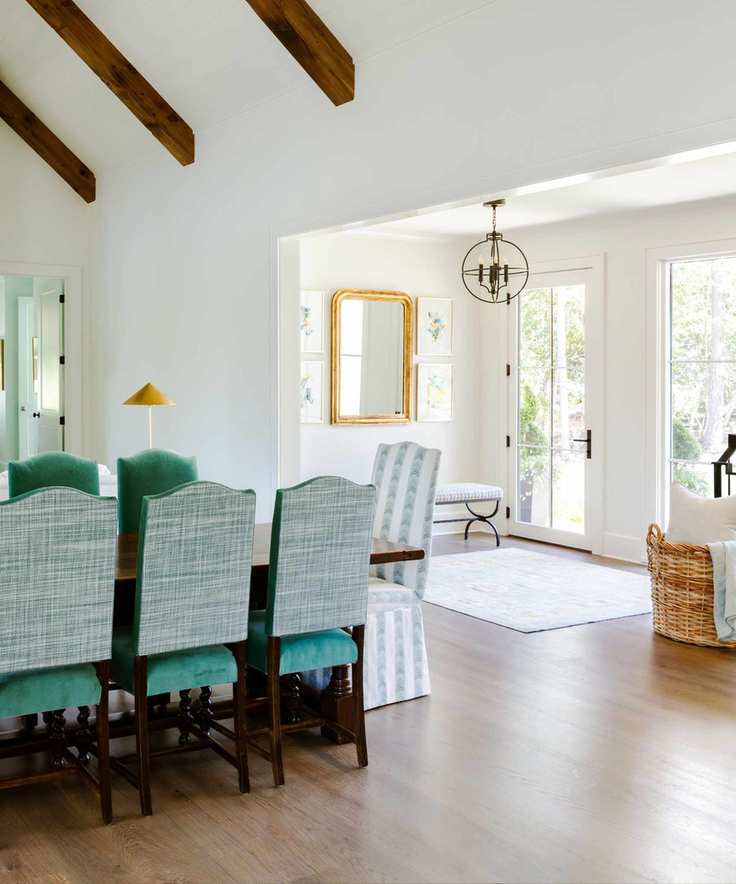 A white entryway and dining room with green velvet chairs.