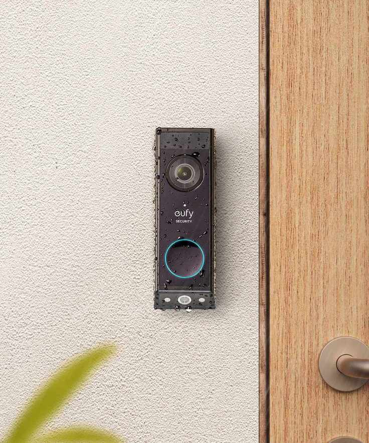 Black eufy e340 video doorbell mounted on concrete wall, next to a wooden front door.