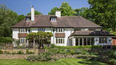 an exterior shot of a large English home in Surrey with a tiered garden surrounded by trees
