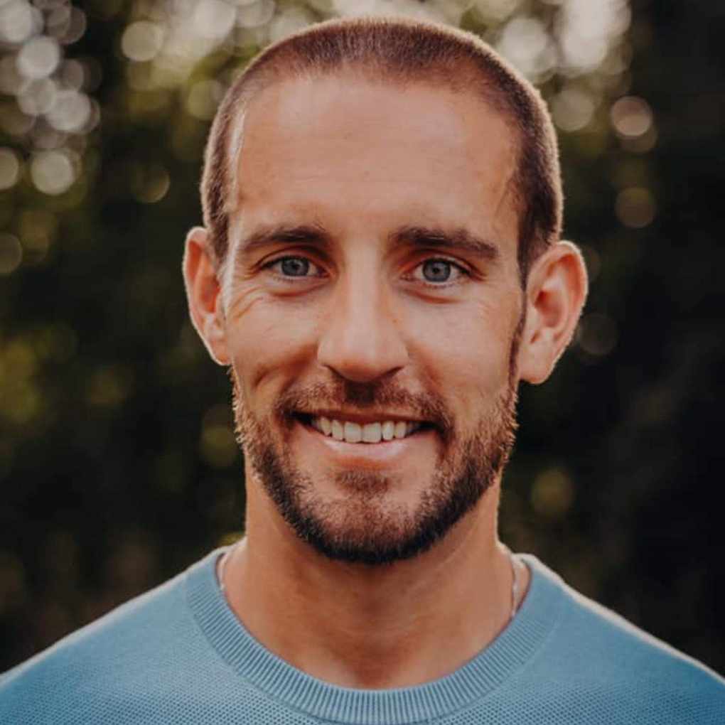 A headshot of Scott Schrader - a man wearing a blue jumper smiling into the camera