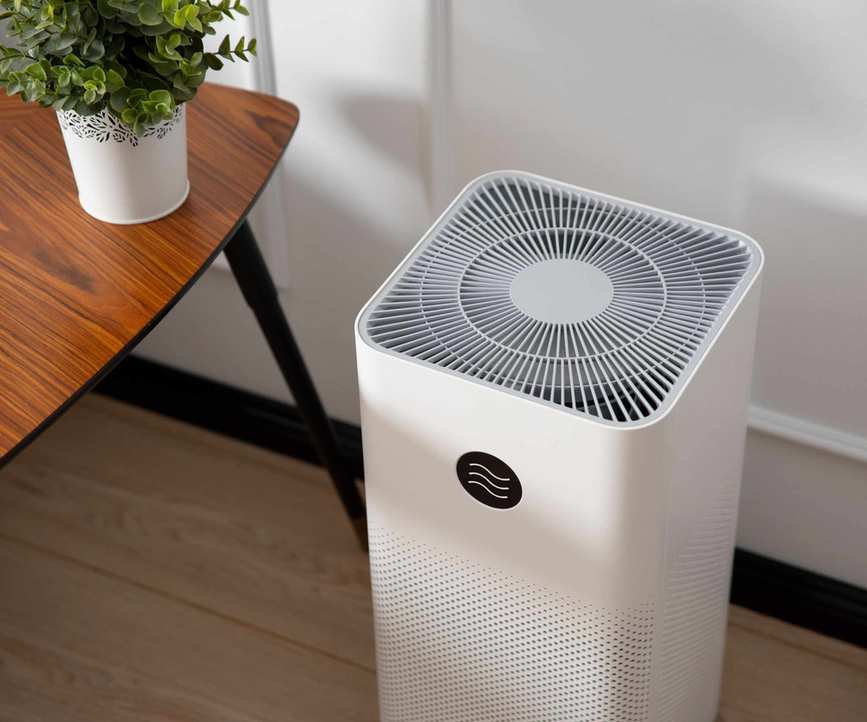 A white air purifier next to a side table and house plant