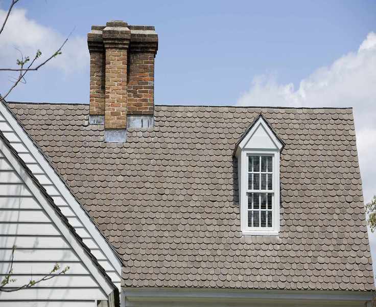 gray tiled roof on large American house with white crittal windows and large central chimney and wood paneled frontage
